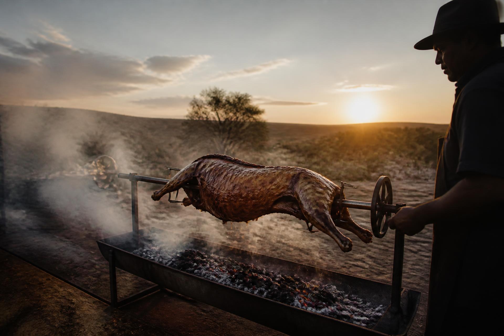 Whole lamb turning on a traditional spit braai over glowing coals
